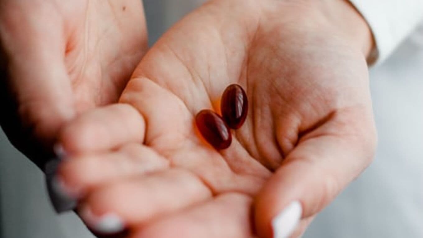 Hands holding out two red/brown capsules